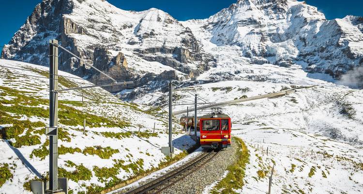 El tren rojo brillante con engranajes sube por las nevadas laderas alpinas bajo la imponente cara norte del Eiger.