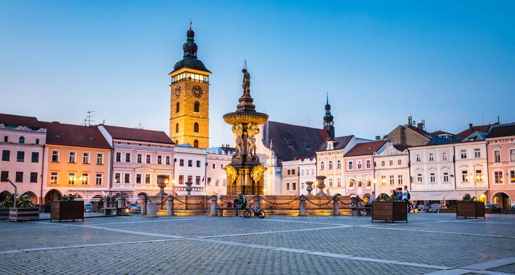 Vista nocturna de la plaza principal de Ceske Budejovice con la Fuente Barroca de Sansón y los edificios históricos iluminados.