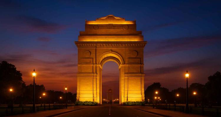 Das India Gate erstrahlt in goldener Beleuchtung vor einem tiefblauen Abendhimmel auf einem leeren Boulevard.