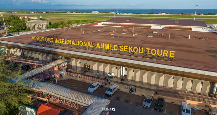 Vista aérea de la terminal del Aeropuerto Internacional Ahmed Sekou Toure con señalización amarilla y vehículos abajo.