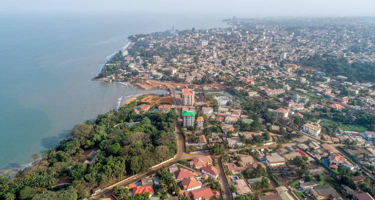Toma aérea desde lo alto de los suburbios de Conakry y la costa con casas rodeadas de árboles.