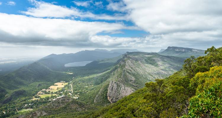 Vue panoramique étendue sur les pics accidentés, les forêts de vallée et le lac des Grampians sous un ciel partiellement nuageux.