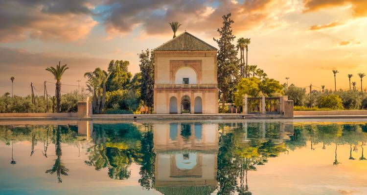 Der Pavillon der Menara-Gärten spiegelt sich bei Sonnenuntergang unter pastellfarbenen Wolken makellos im ruhigen Wasser von Marrakesch.