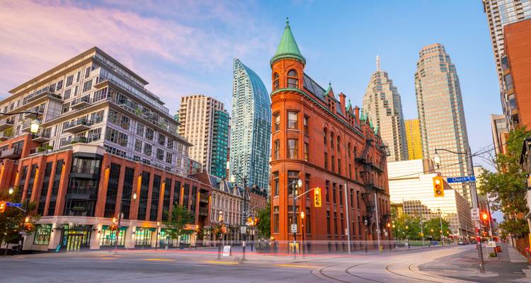 Das historische rote Backsteingebäude Gooderham Building, umgeben von modernen Wolkenkratzern in der Innenstadt von Toronto, getaucht in weiches Sonnenlicht der Morgenröte.