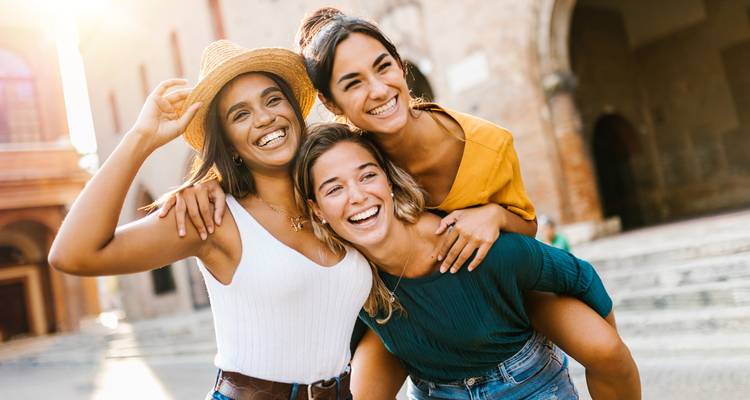 Drie vrolijke vrienden lachen samen in warm zonlicht tegen historische Italiaanse architectuur.