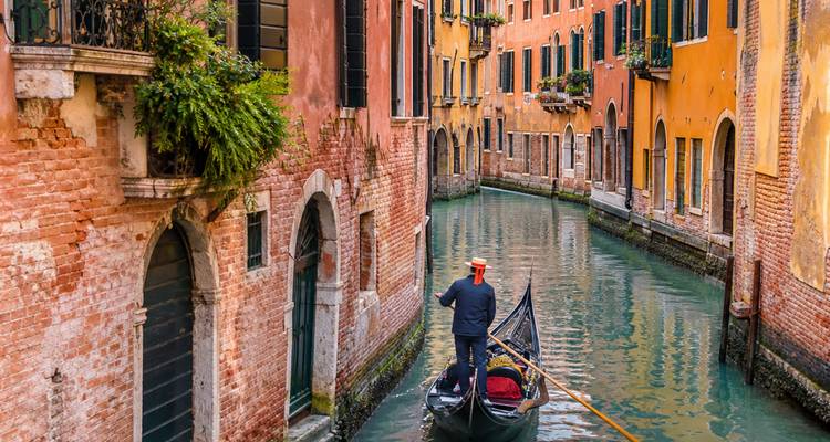Un gondolier navigue dans une élégante gondole noire à travers un étroit canal vénitien bordé de bâtiments historiques colorés se reflétant dans l'eau calme.