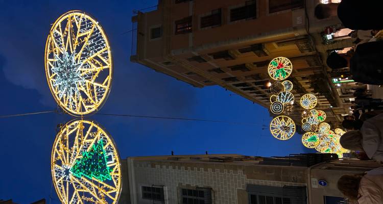 Scène nocturne d'une rue avec de grandes lumières de Noël circulaires suspendues au-dessus des foules entre les bâtiments historiques de Barcelone.