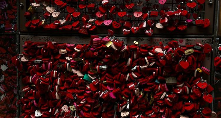 Mur dense de cadenas d'amour en forme de cœur rouge attachés à une grille métallique.