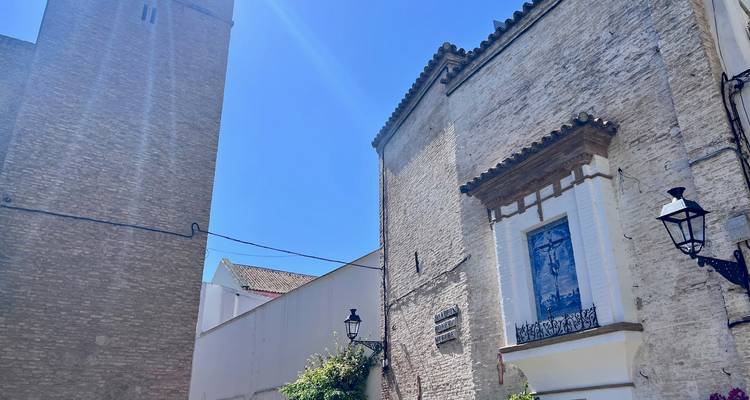 Tour d'église en briques aux teintes ensoleillées et bâtiments adjacents avec effet de lumière parasite dans un ciel bleu dégagé.