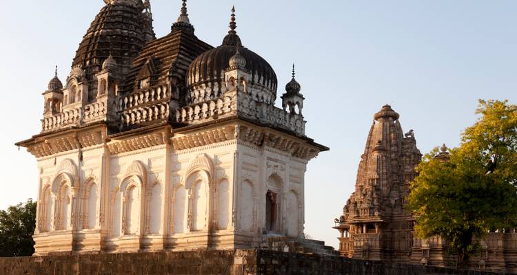 Kontrastierende weiße und sandsteinfarbene Tempel stehen nebeneinander in Khajuraho unter klarem Morgenlicht.
