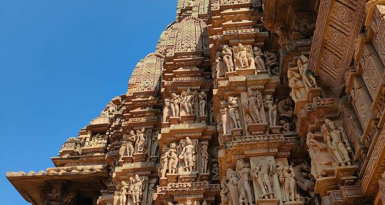 Nahaufnahme aus schrägem Blickwinkel auf die Türme des Khajuraho-Tempels mit aufwändigen Statuen vor lebendigem blauem Himmel.