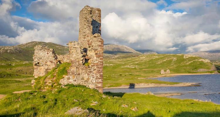 Vista más cercana de las ruinas del Castillo de Ardvreck contra las Tierras Altas ondulantes y nubes dispersas.