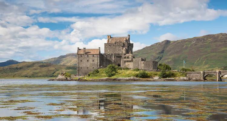 El castillo de piedra de Eilean Donan se sienta en una pequeña isla de mareas reflejada en las tranquilas aguas del lago contra colinas verdes.