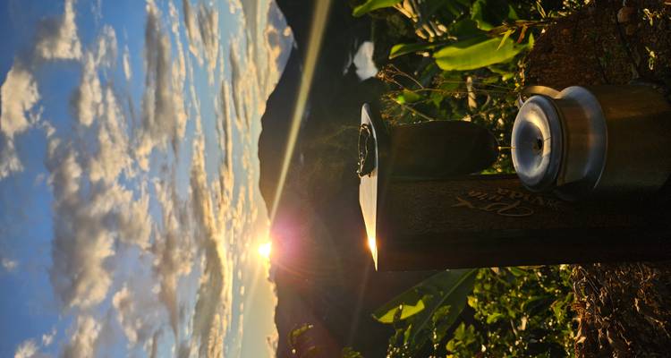 Configuración para preparar café en una ladera de montaña al amanecer con un valle y un embalse abajo.