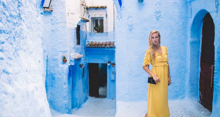 Mujer con vestido amarillo parada en un callejón azul vibrante del casco antiguo de Chefchaouen.
