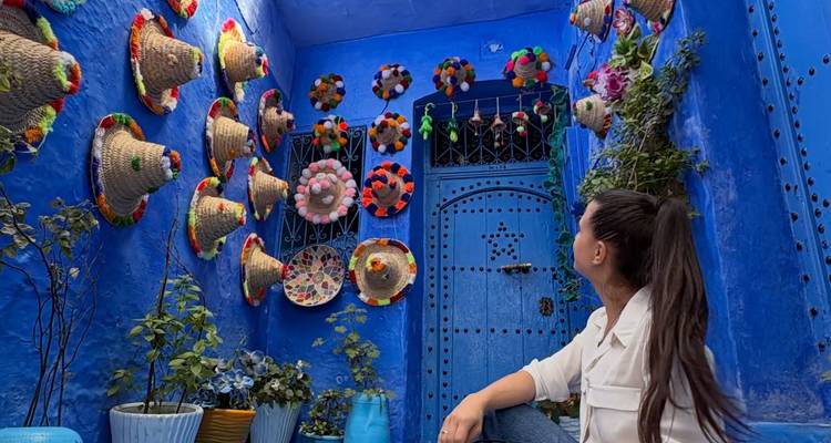 Viajero admirando sombreros de pompones coloridos adornando una pared de patio azul brillante en Chefchaouen.