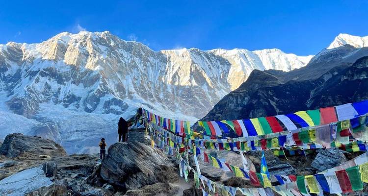 Gebedsvlaggen wapperen voor de dramatische ijswanden van Annapurna Base Camp onder een helder blauwe lucht.