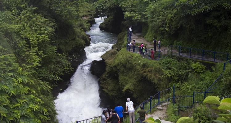 Weelderige groene kloof met een krachtige waterval en bezoekers die toekijken vanaf blauwe leuningen