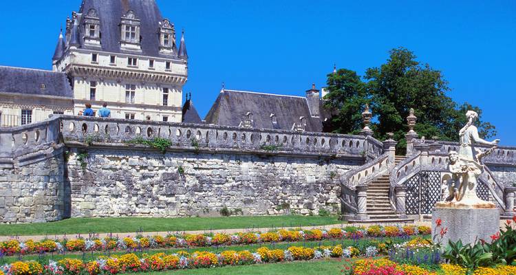 Elegante terraza de castillo con balaustrada de piedra, canteros de flores coloridas y una escultura contra un hermoso cielo azul de verano.