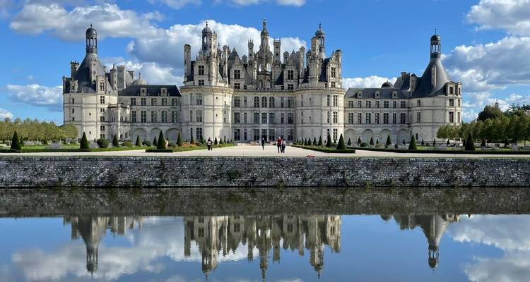 El Château de Chambord del Loira se refleja perfectamente en un foso tranquilo bajo un cielo azul vivido y nubes esponjosas.
