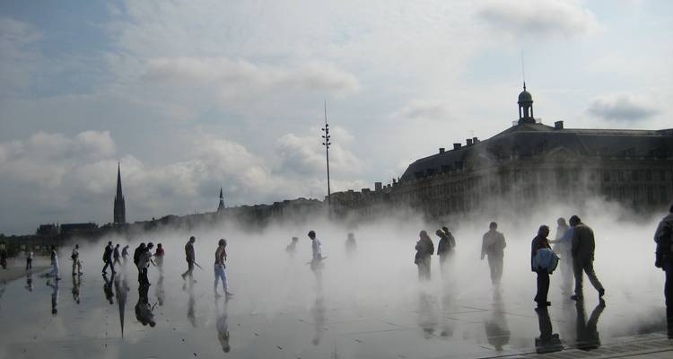 Gesilhouetteerde voetgangers waden door een mistig wateroppervlak voor de Place de la Bourse in Bordeaux.