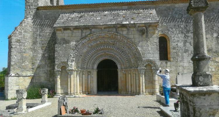 Romaans kerkportaal met rijkelijk uitgesneden concentrische bogen terwijl een bezoeker de voorgevel fotografeert.