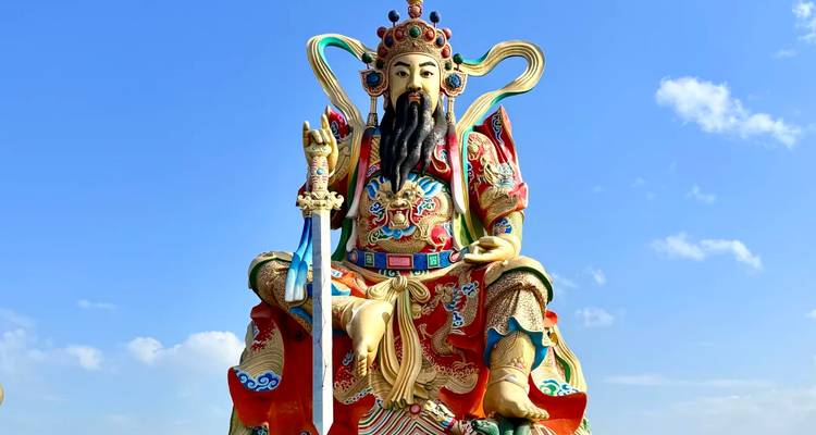 Bunte überlebensgroße Statue einer taoistischen Gottheit vor strahlend blauem Himmel.