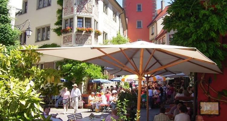 Belebter Fußgängerplatz in einer mittelalterlichen deutschen Stadt, gefüllt mit Cafés, Schirmen und Touristen.