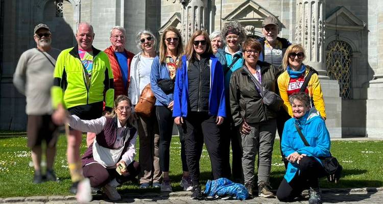 Eine Gruppe von Radtouristen posiert an einem sonnigen Tag vor einer historischen Kathedrale.