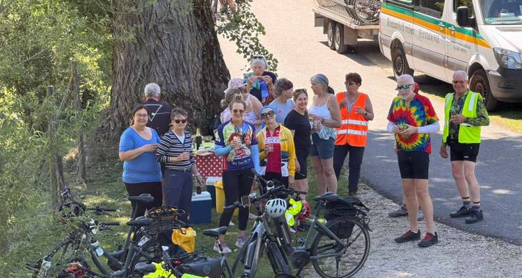 Radfahrer halten an einer Raststätte neben einem Supportfahrzeug und geparkten E-Bikes an, um eine Verpflegungspause einzulegen.