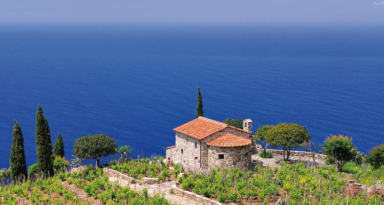 Casa de piedra de granja encaramada sobre viñedos en terrazas con el profundo mar Mediterráneo azul más allá.