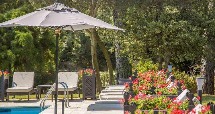 Eleganter Außenpoolbereich mit Liegen, Sonnenschirmen und leuchtenden Blumenkästen, umgeben von hohen Bäumen.