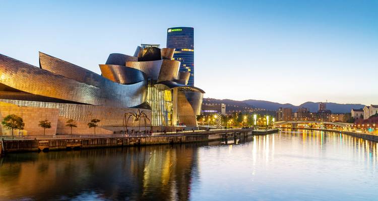 Vue au crépuscule du Musée Guggenheim Bilbao se reflétant dans la rivière Nervión avec les lumières de la ville