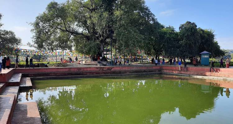 Étang vert à Lumbini avec des drapeaux de prière colorés tendus au-dessus et des visiteurs à proximité