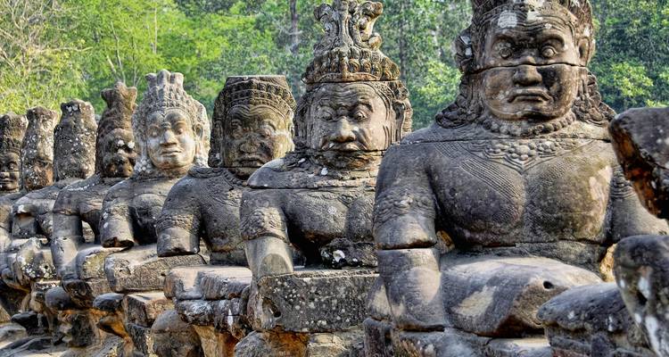 Reihe von verwitterten steinernen Wächterfiguren, die eine Brücke am Eingang zu Angkor Thom säumen.
