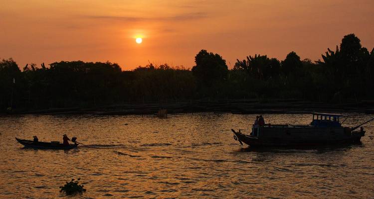 Silhouetten van kleine bootjes op een brede rivier bij zonsondergang met een oranje lucht boven de Mekong.