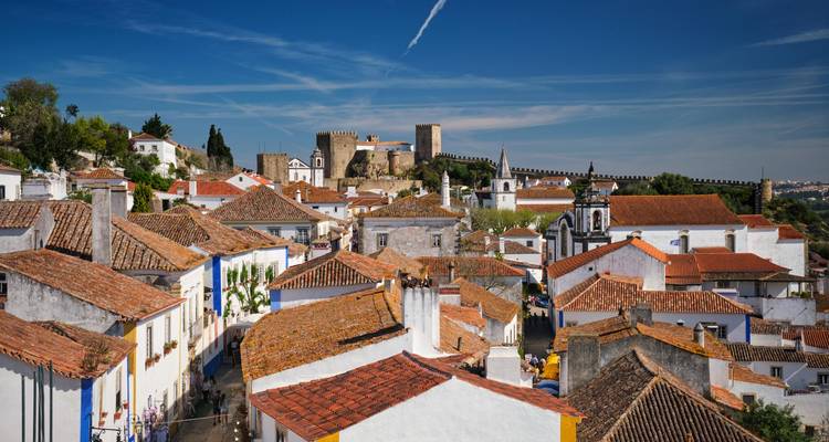 Azoteas brillantemente iluminadas del casco antiguo de Óbidos bajo un cielo azul profundo con el castillo de fondo