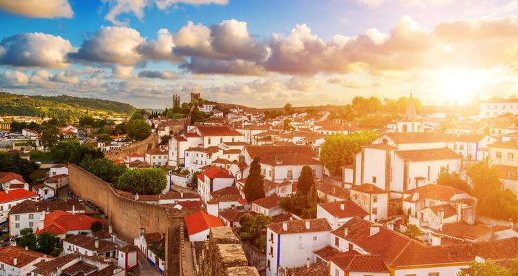 Puesta de sol dorada iluminando con luz cálida el pueblo amurallado de Óbidos y el paisaje ondulado