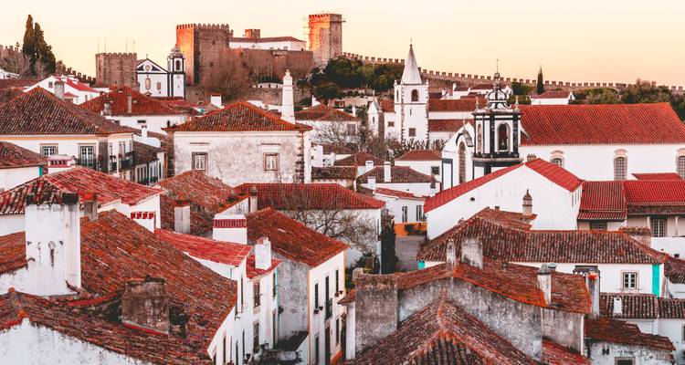 Luz suave del amanecer sobre los tejados blancos y rojos de Óbidos con las murallas del castillo a lo lejos