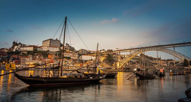 Barcos rabelo tradicionales amarrados en el río Douro al atardecer con el Puente Dom Luís I iluminado