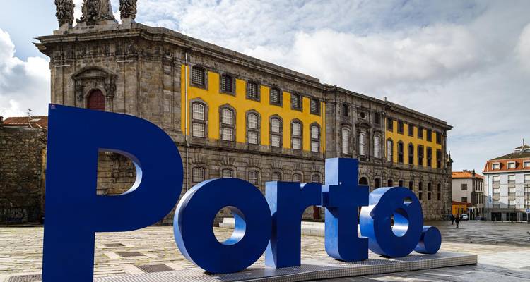 Gran letrero azul de Porto en plaza histórica con edificio clásico de piedra de fondo
