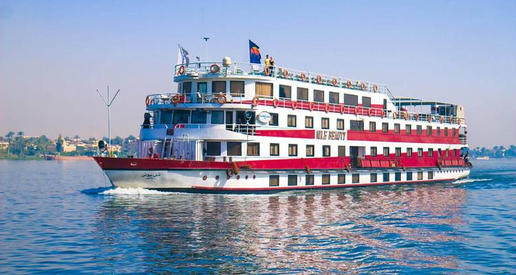 Un bateau de croisière multi-ponts sur le Nil aux rayures rouge et blanc navigue sans à-coups sur une eau bleue calme.