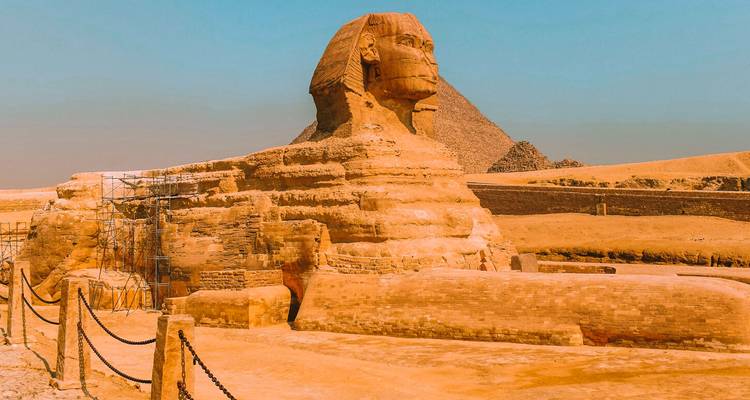 Profil latéral du Grand Sphinx avec des échafaudages désertiques et une pyramide partiellement visible en arrière-plan.