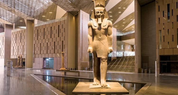 Hall intérieur du Grand Musée égyptien présentant une statue colossale de Pharaon reflétée dans un bassin peu profond.