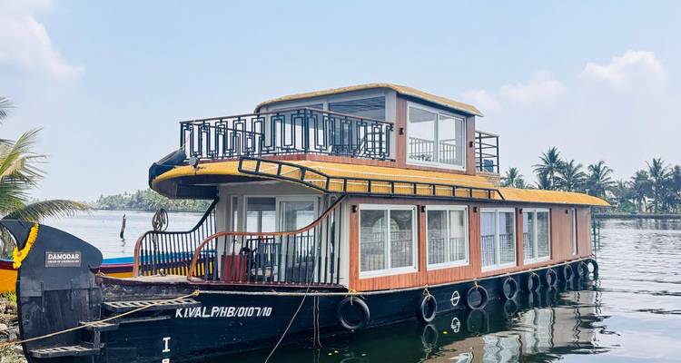 Modernes zweistöckiges Hausboot aus Kerala, das auf ruhigen Backwaters unter leichten Wolken vertäut ist.
