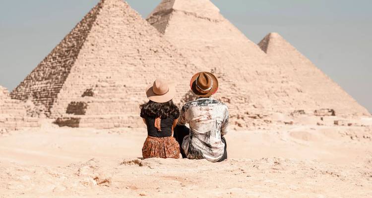 Un jeune couple assis sur le sable du désert admire les Grandes Pyramides de Giza.