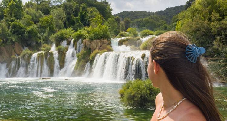 Frau blickt auf die gestuften Wasserfälle von Skradinski Buk, die in smaragdgrüne Pools im Nationalpark Krka herabstürzen