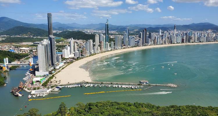 Vue aérienne de la ligne d'horizon de Balneário Camboriú s'incurvant autour de la baie sablonneuse avec marina et collines boisées