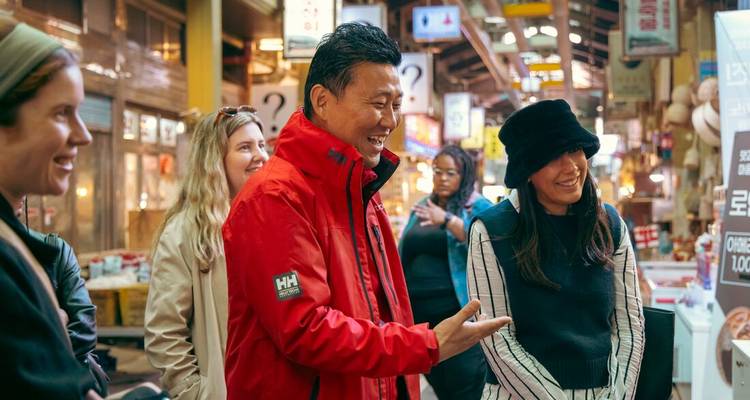 Les visiteurs partagent un moment de rire avec un guide à l'intérieur d'un marché couvert coréen animé.