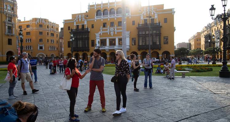 Drukke Plaza de Armas met gele koloniale gebouwen en toeristen die in de middagzon met elkaar kletsen